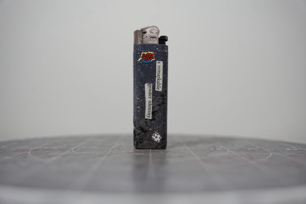 Hand-collaged lighter with navy speckled ground, cut-paper florals and the text "a remarkable gender identity"