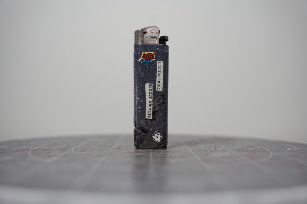 Hand-collaged lighter with navy speckled ground, cut-paper florals and the text "a remarkable gender identity"