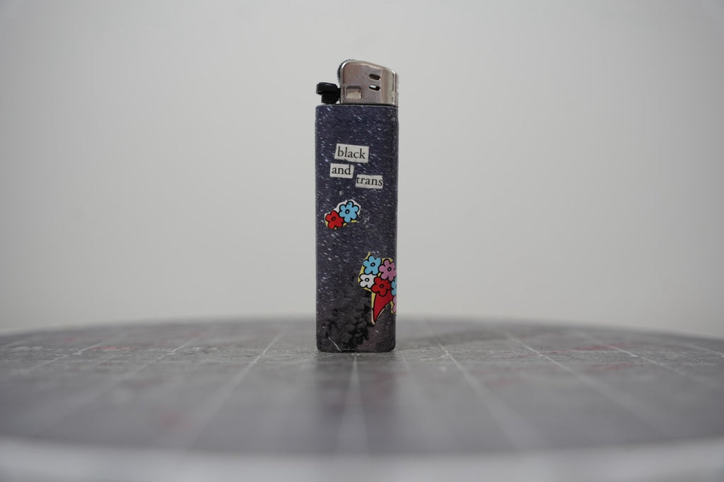 Reverse side of the collaged lighter reading "black and trans" with cut-paper flower bouquets