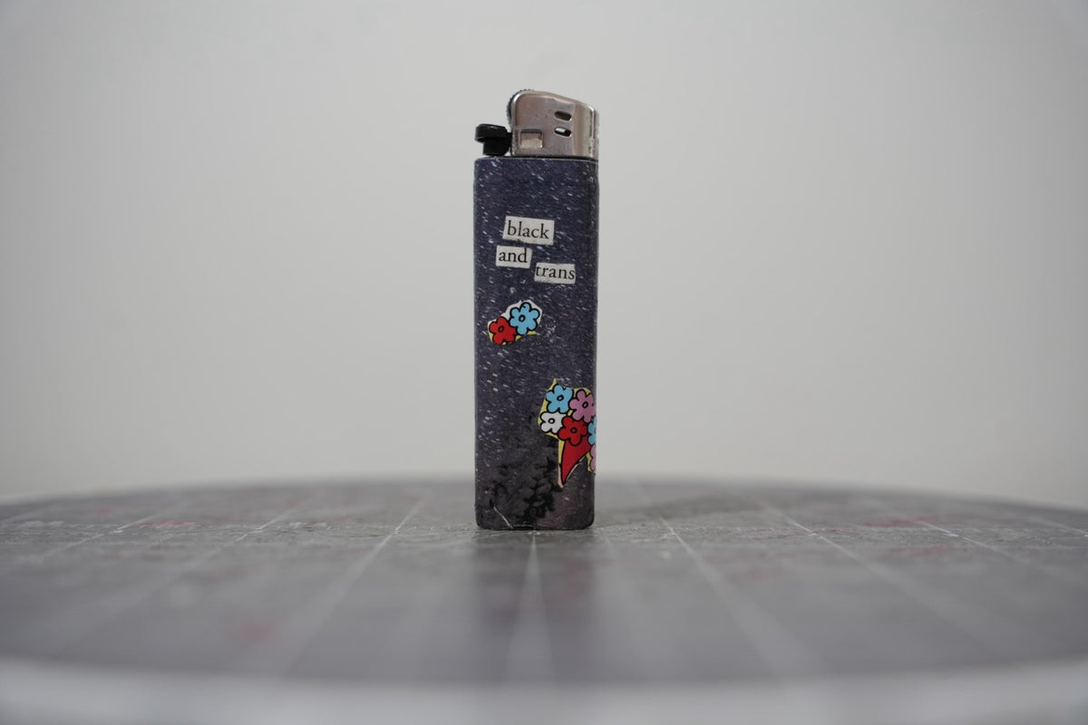 Reverse side of the collaged lighter reading "black and trans" with cut-paper flower bouquets