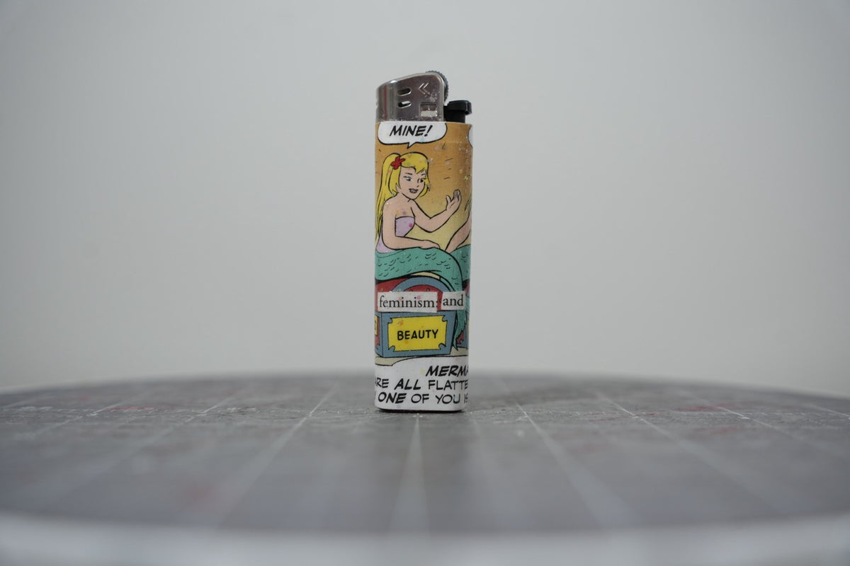 Hand-collaged lighter made from Disney comic book paper, showing a mermaid with cut-paper text "feminism and beauty"