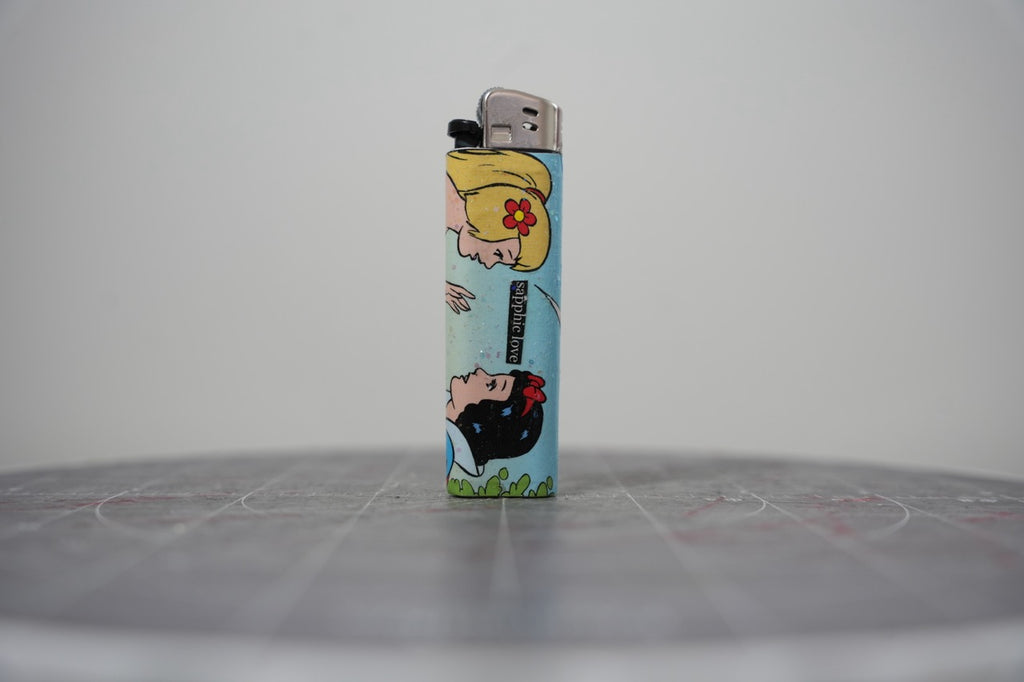 Hand-collaged lighter made from Disney comic book paper, two princesses with a cut-paper clipping reading "sapphic love"