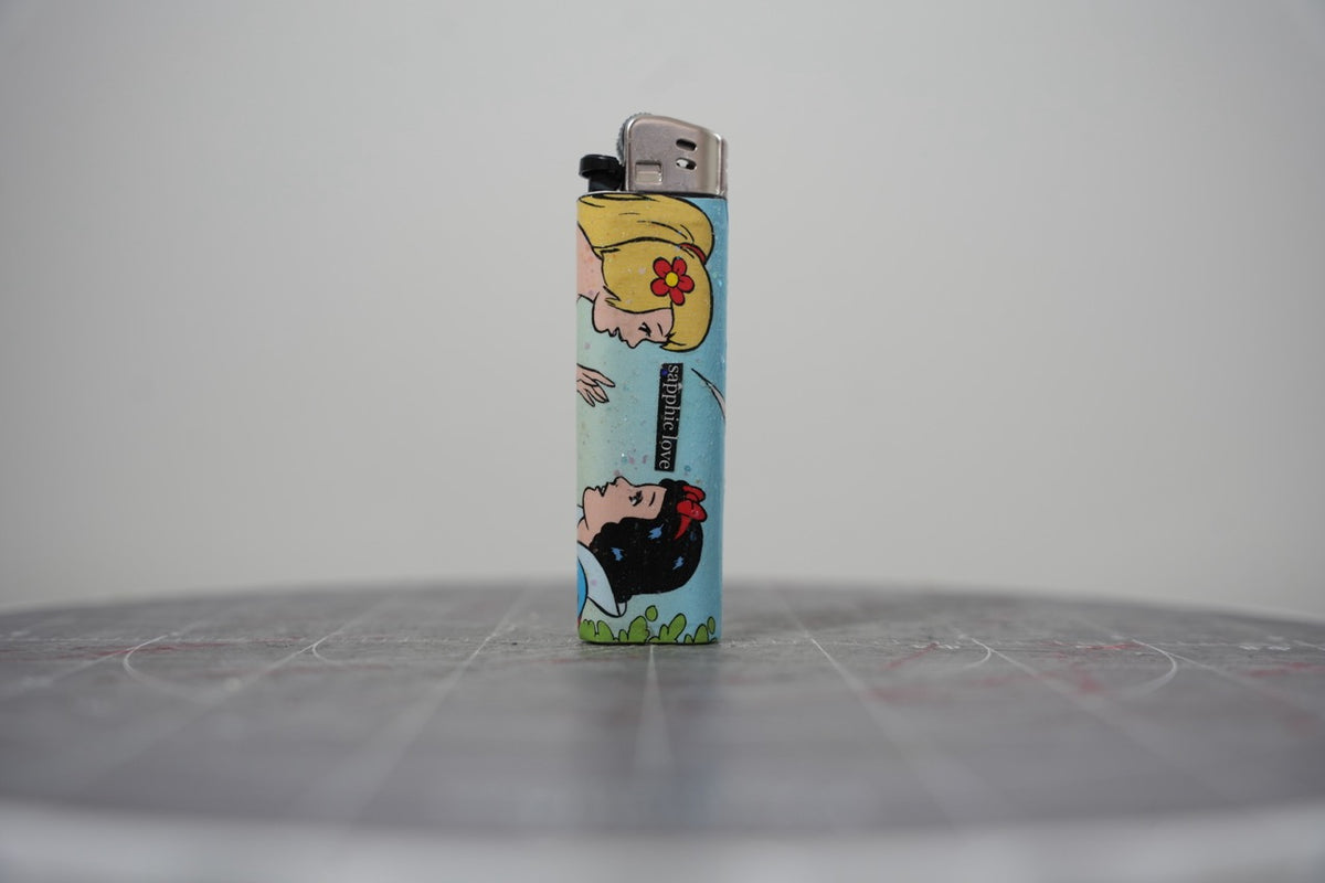 Hand-collaged lighter made from Disney comic book paper, two princesses with a cut-paper clipping reading "sapphic love"