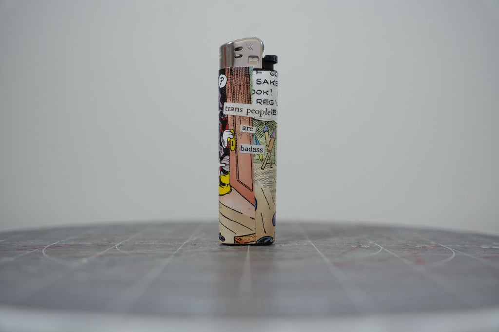 Front of a handmade collage lighter made from vintage Disney comic book paper, Mickey Mouse with cut-paper text reading trans people are badass
