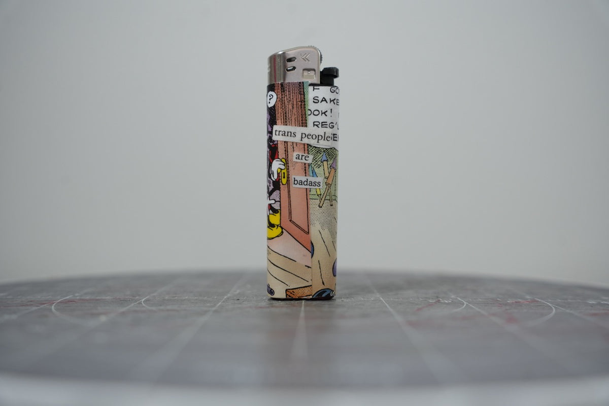 Front of a handmade collage lighter made from vintage Disney comic book paper, Mickey Mouse with cut-paper text reading trans people are badass