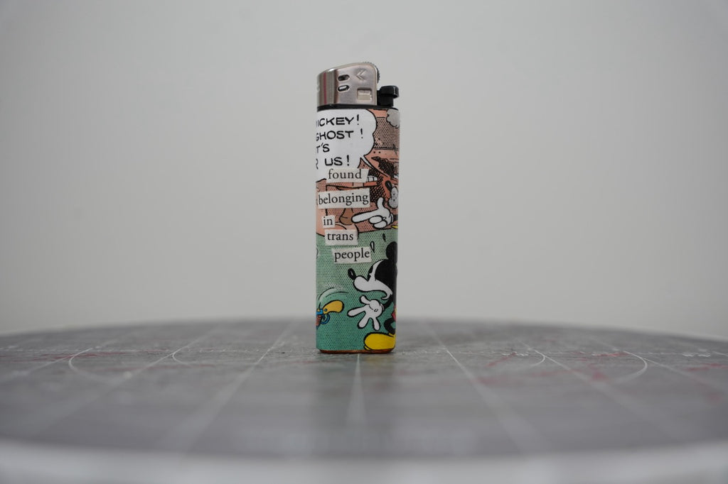 Front of a handmade collage lighter made from vintage Disney comic book paper, cut-paper text reading found belonging in trans people