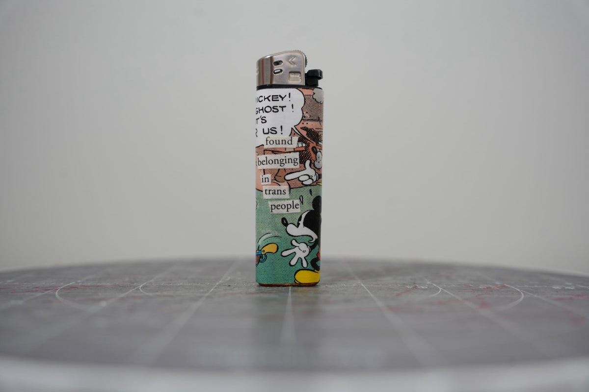 Front of a handmade collage lighter made from vintage Disney comic book paper, cut-paper text reading found belonging in trans people