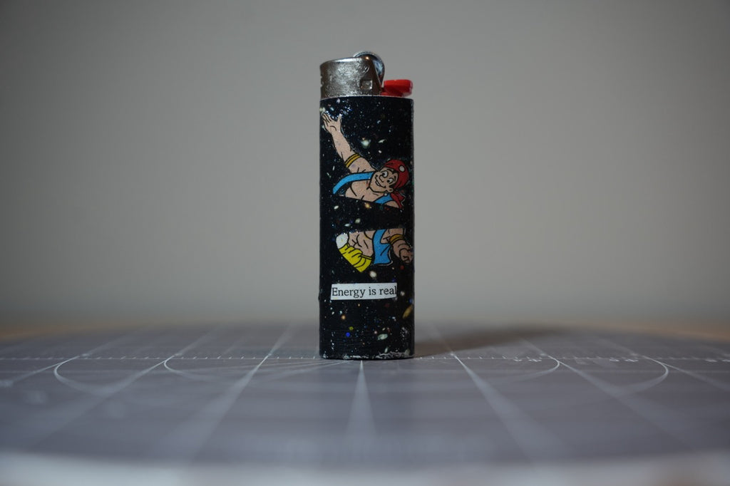 Handmade collage lighter, black glittered space with a cartoon man in a red bandana and the words energy is real