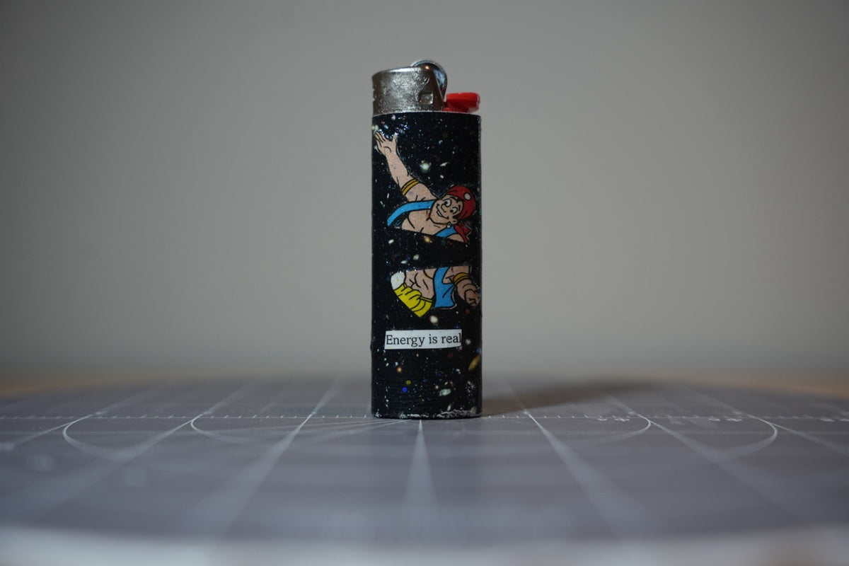Handmade collage lighter, black glittered space with a cartoon man in a red bandana and the words energy is real